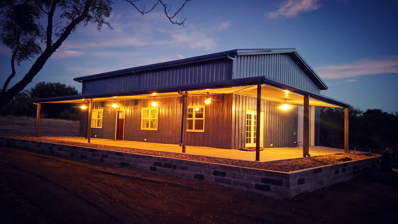 Barndominium lit up at night against the sunset.